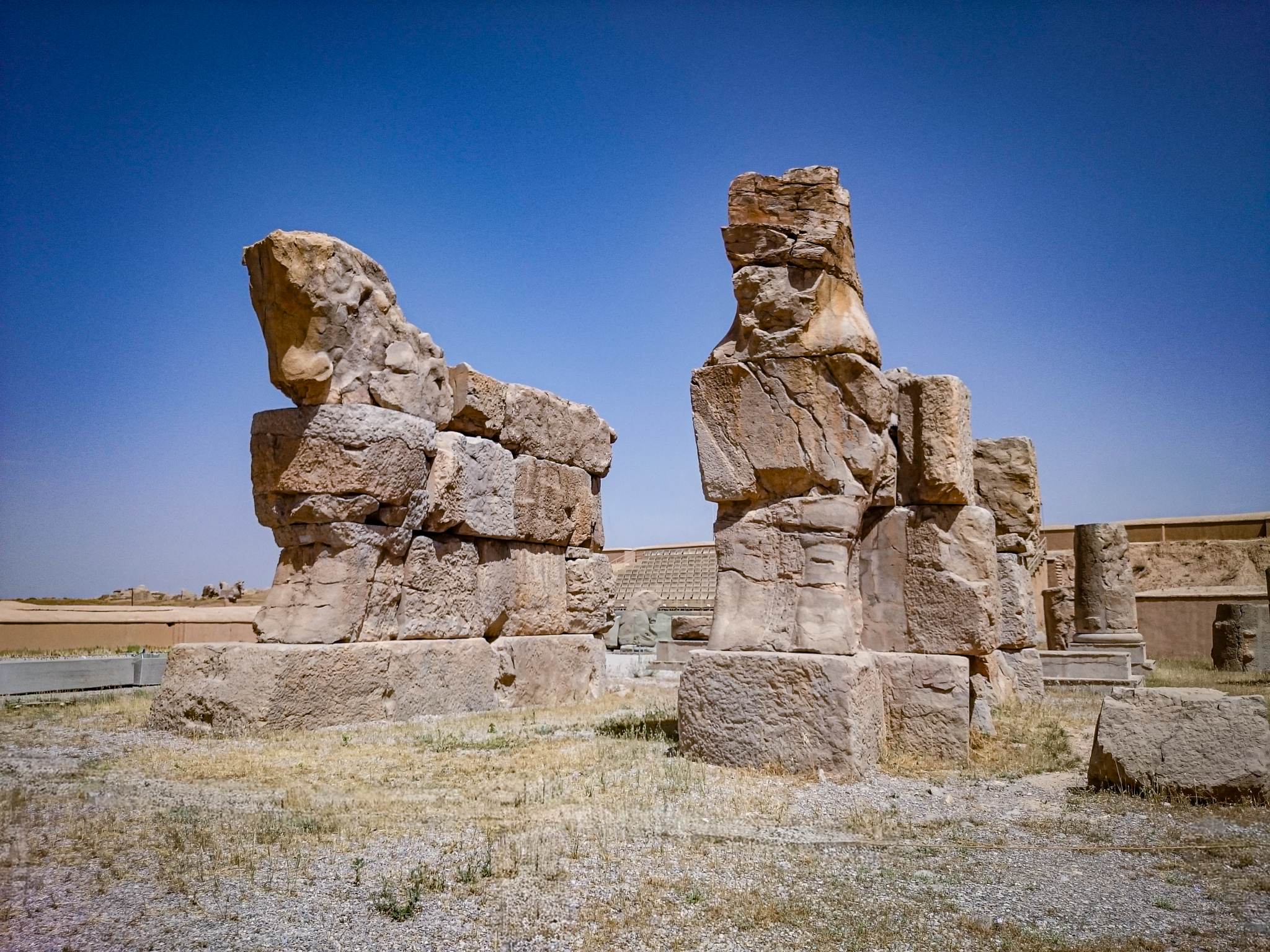 Close-up of two heavily damaged, fragmented ancient bull statues at Persepolis. The weathered stone pieces are stacked, showing remnants of the massive sculptures against a clear sky.