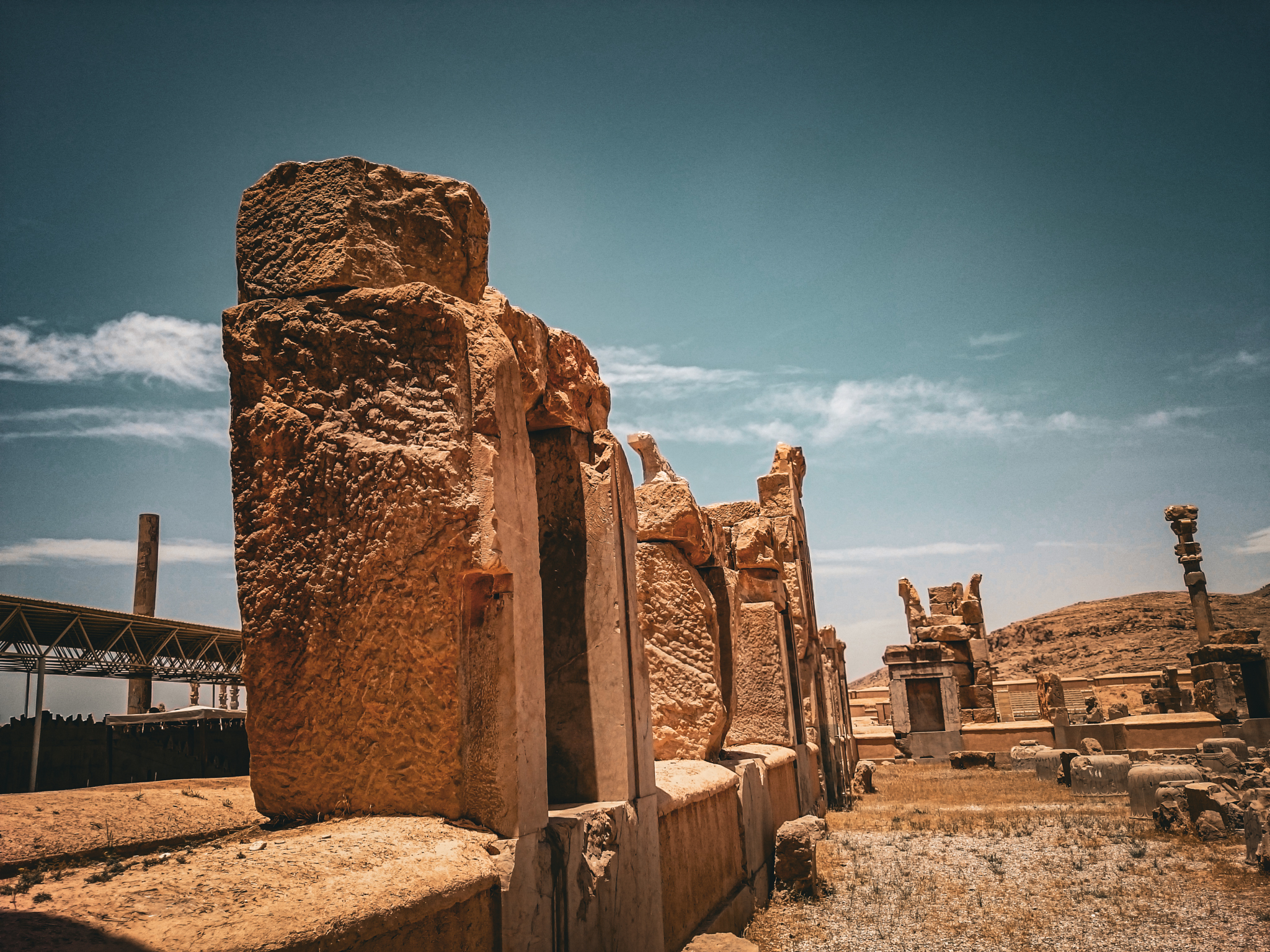 Low-angle view of the ancient stone wall ruins inside the Hall of 100 Columns at Persepolis, showing weathered limestone texture against a clear sky.
